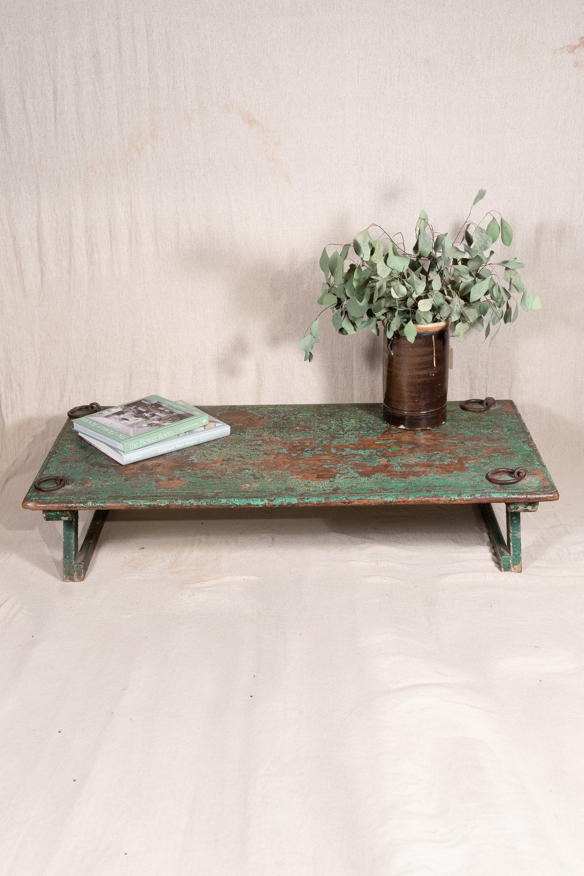 Low wooden bajot table with distressed green paint, angled legs and metal corner rings, possibly repurposed from an old gate or door.