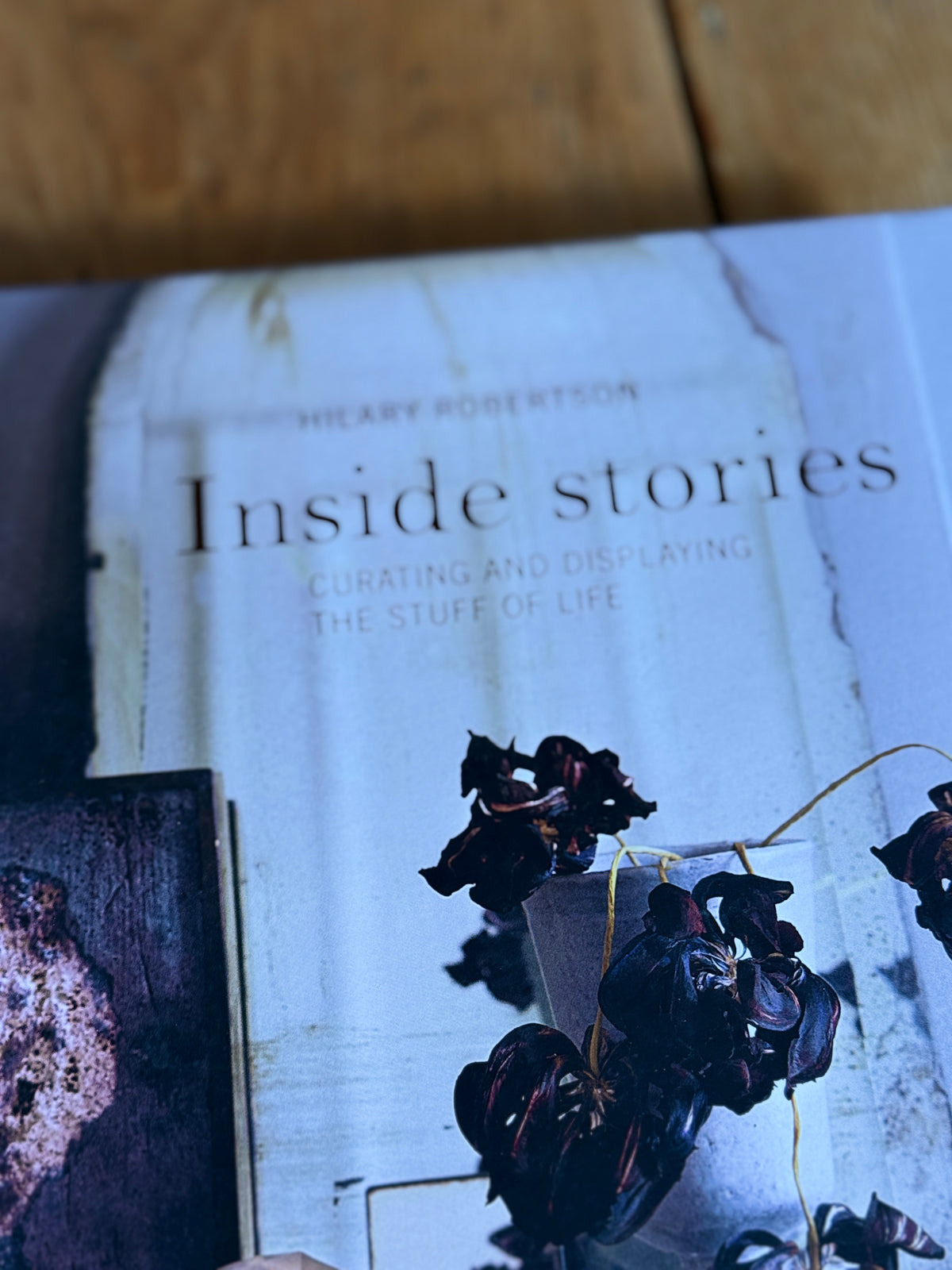 A close-up of a book titled 'Inside stories' by Heavy Robertson, featuring a light blue-gray cover with dark dried flowers and a rustic wooden surface in the background.
