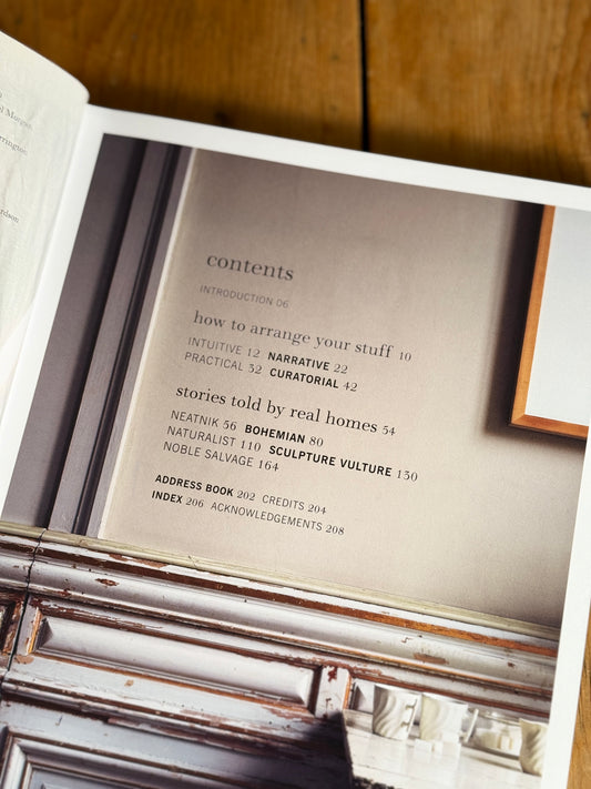 An open book showing a printed table of contents page, photographed on a wooden surface with part of a distressed wooden chair visible in the foreground.