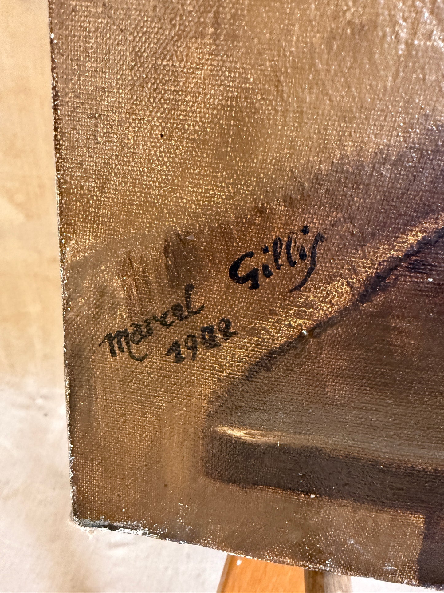 Close-up of a textured canvas painting corner showing a black painted signature reading 'Marcel Gilliy' and the year '1932' on a brown and dark gray painted surface.