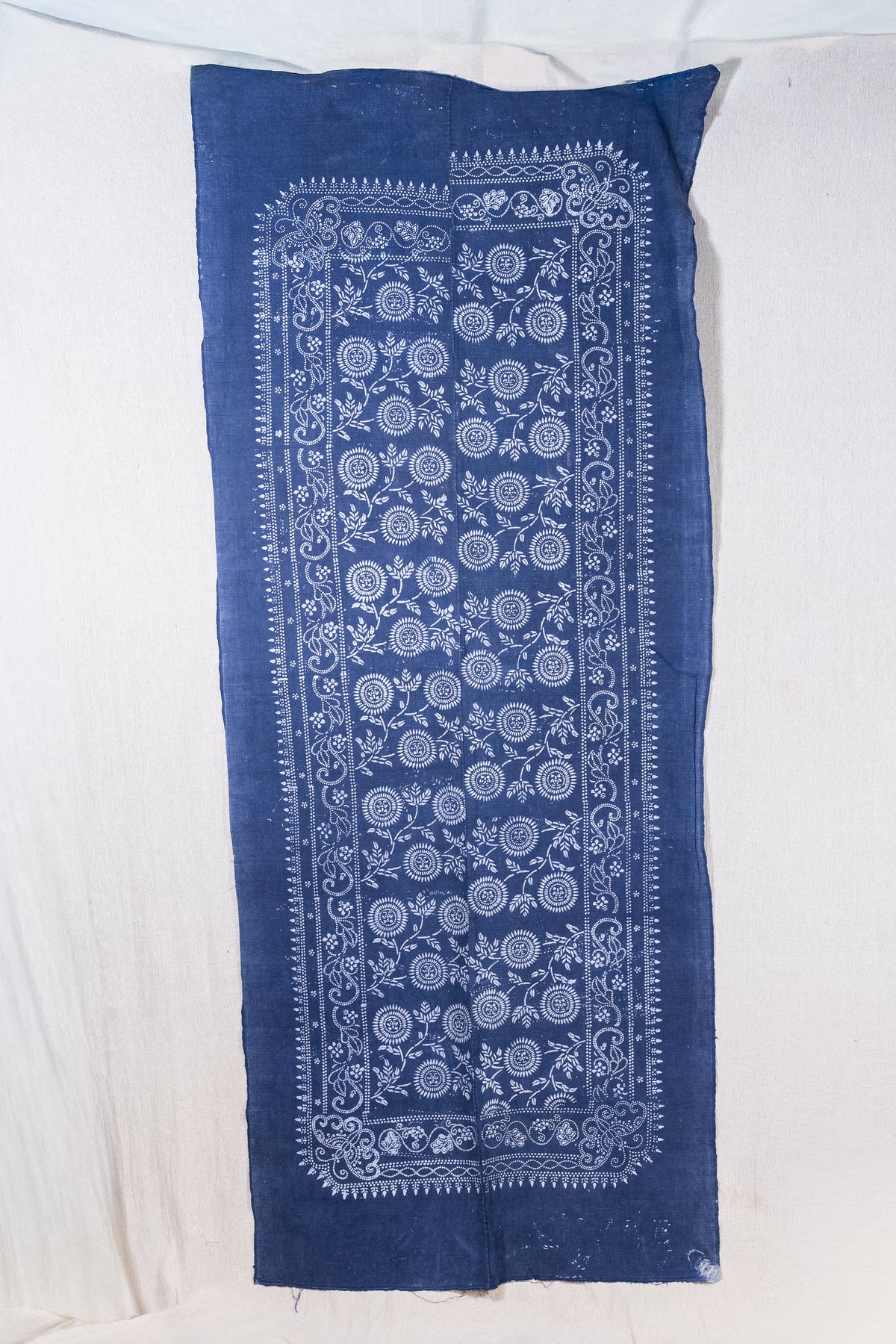 A rectangular indigo blue fabric panel with a white printed floral and geometric border pattern, laid flat on a white fabric background.