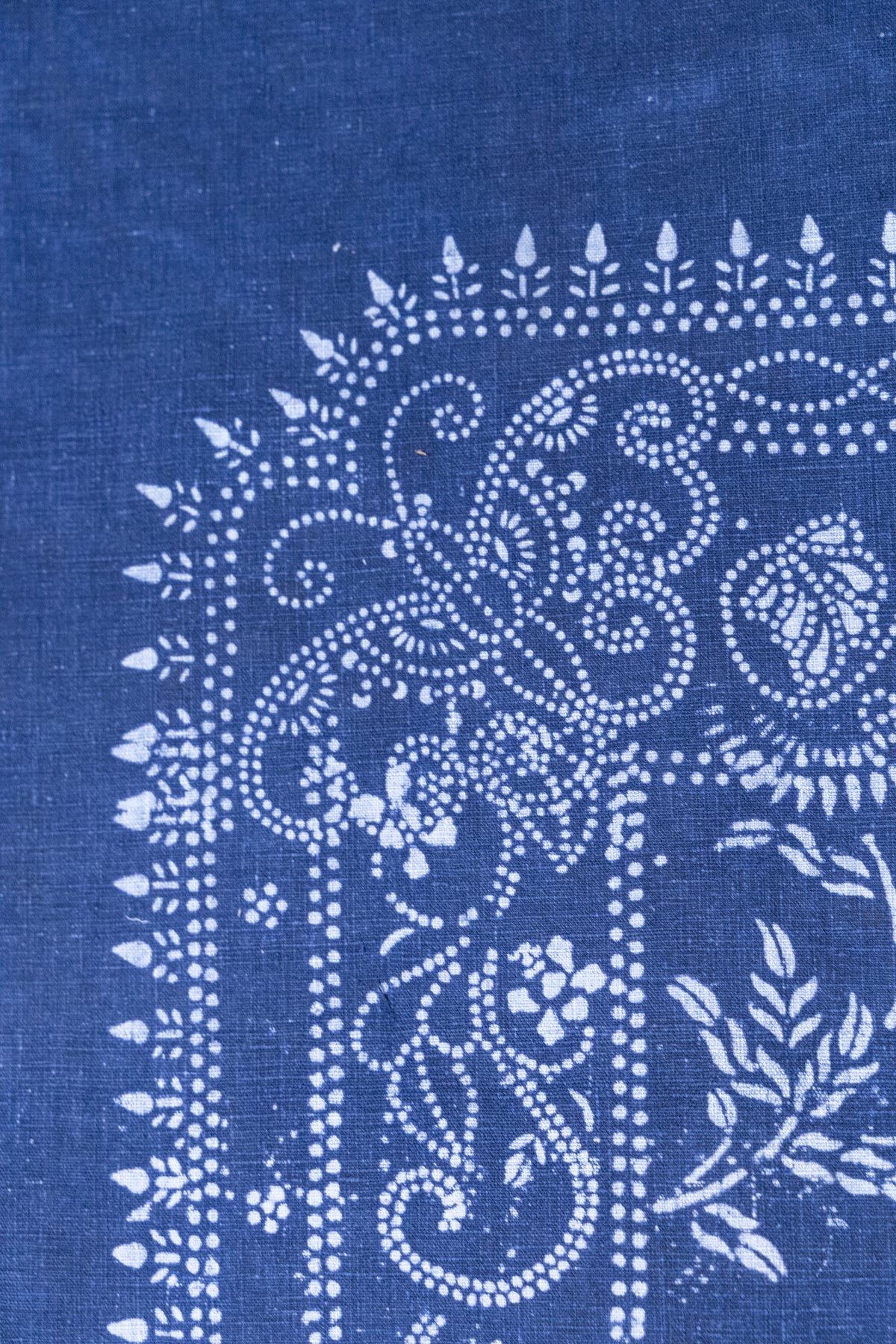 A close-up of indigo blue fabric with a white hand-block printed floral and scroll pattern.