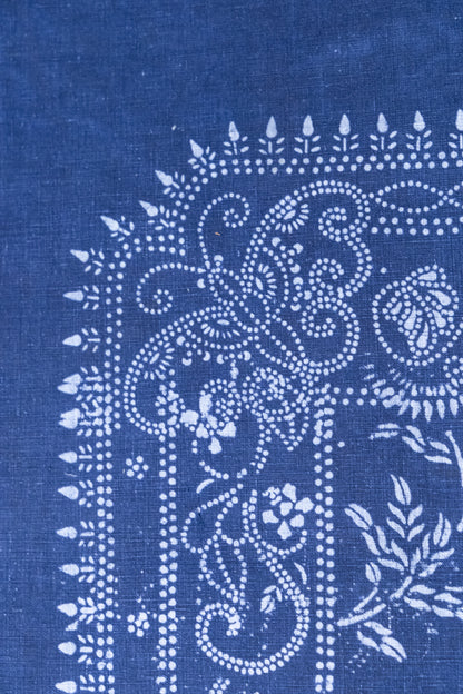 A close-up of indigo blue fabric with a white hand-block printed floral and scroll pattern.