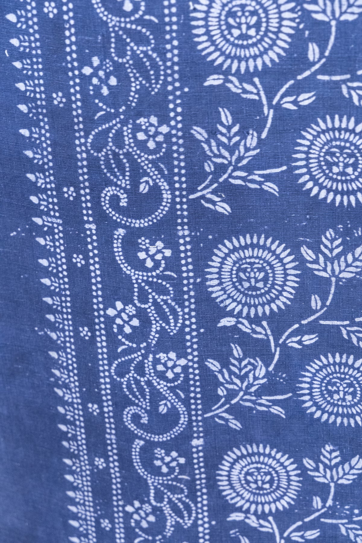 A close-up of a blue fabric with white printed floral and vine patterns, showing the textile texture and design details.