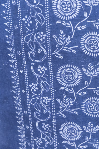 A close-up of a blue fabric with white printed floral and vine patterns, showing the textile texture and design details.