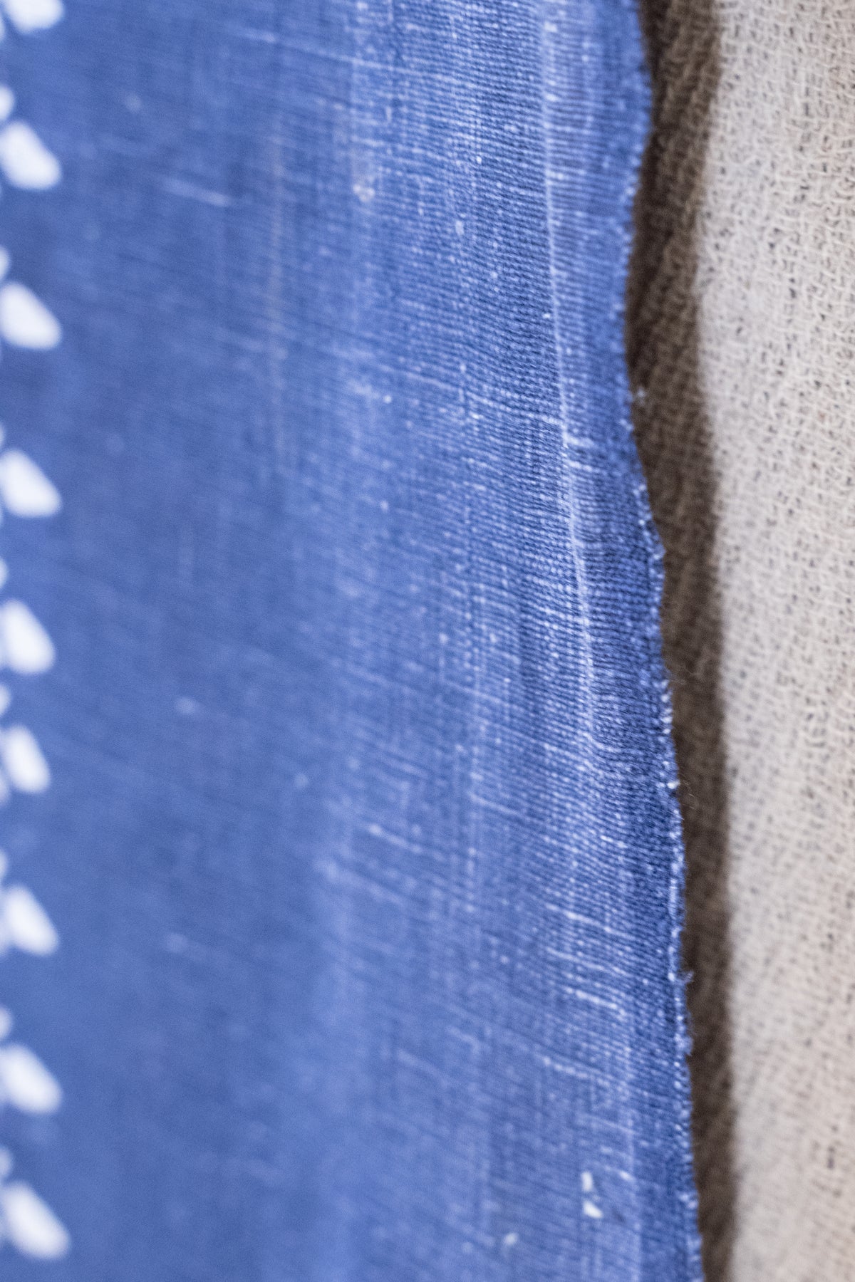 Close-up of a blue woven fabric with white dotted pattern along the edge, next to a beige textured fabric.