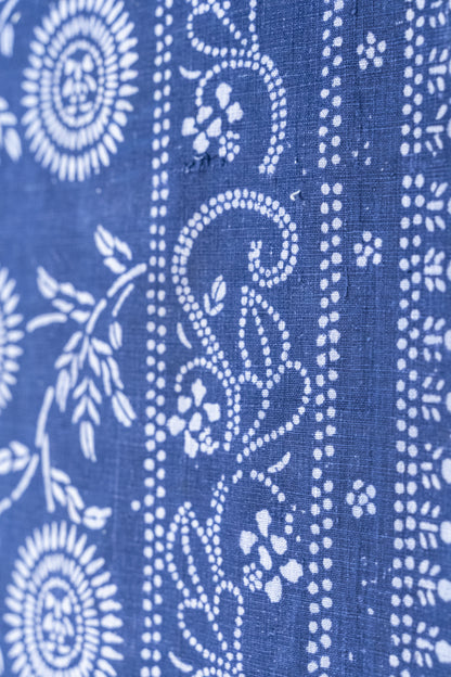 A close-up of indigo blue fabric with white block-printed floral and scroll patterns.