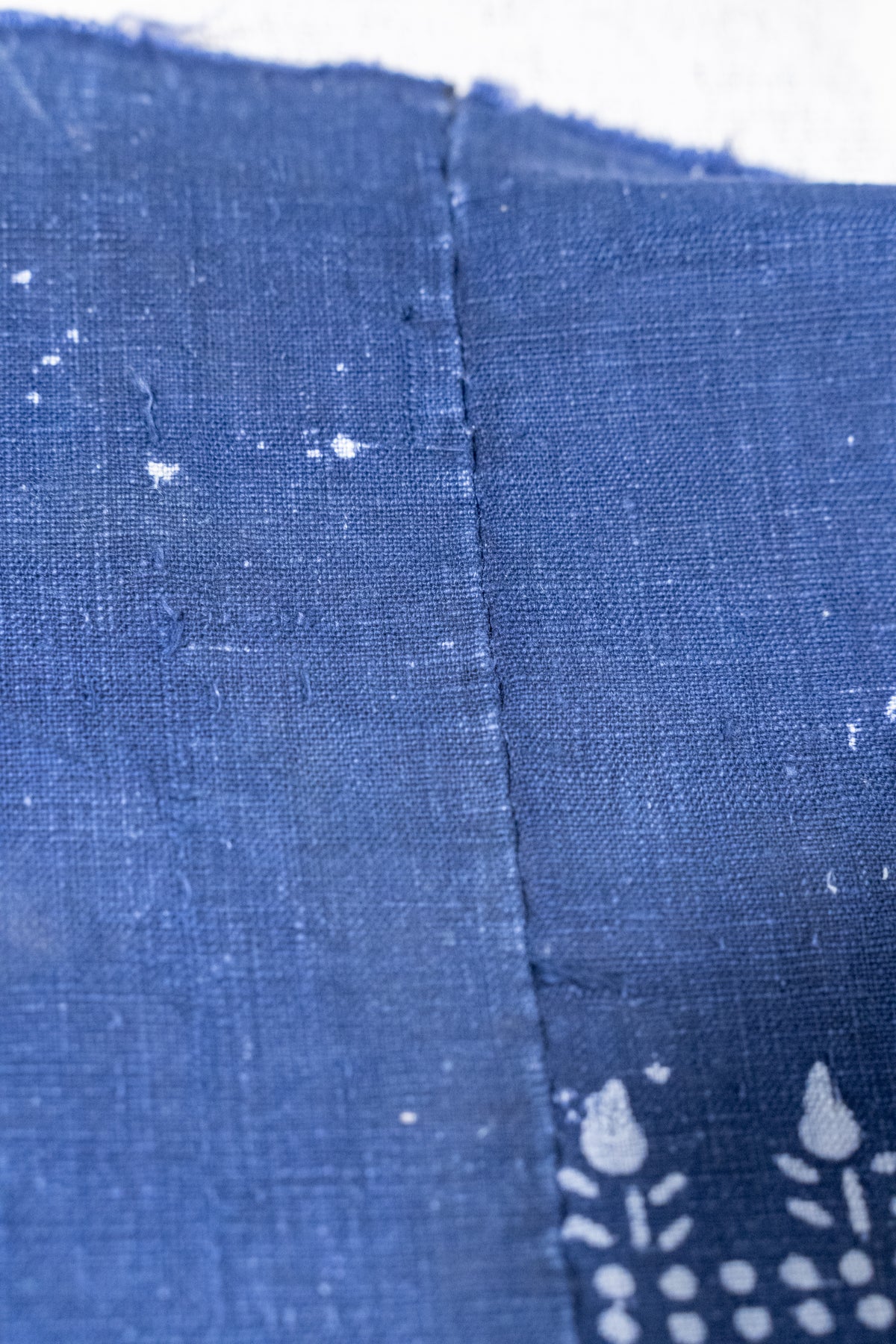 Close-up of indigo blue fabric with a visible center seam and white floral block-print style motifs near the bottom right.