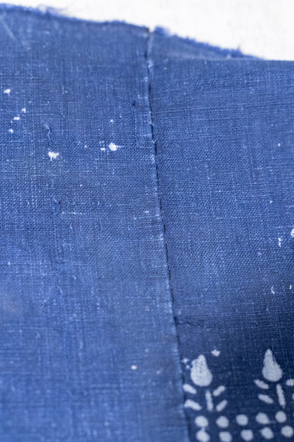 Close-up of indigo blue fabric with a visible center seam and white floral block-print style motifs near the bottom right.