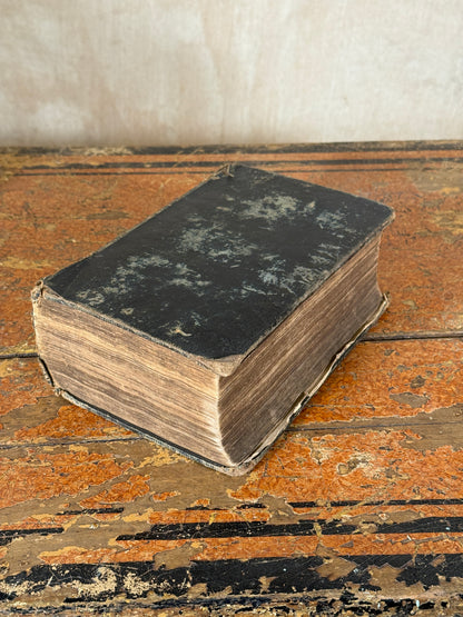 Vintage book with black cover and worn edges on a textured surface