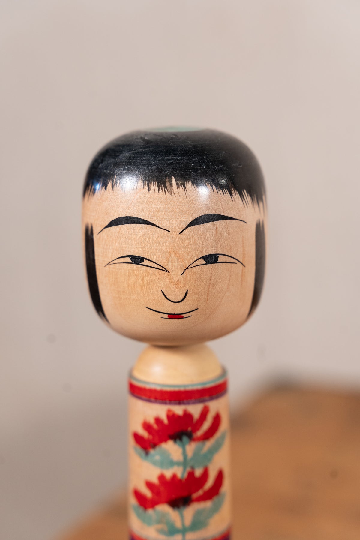 A traditional Japanese kokeshu wooden doll with a hand-painted face and floral pattern on its body, set against a neutral background.