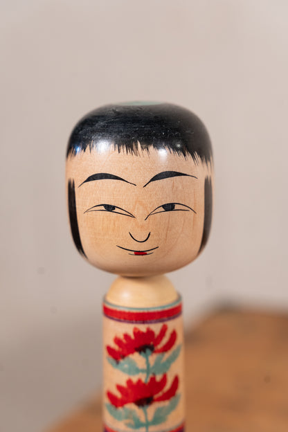 A traditional Japanese kokeshu wooden doll with a hand-painted face and floral pattern on its body, set against a neutral background.