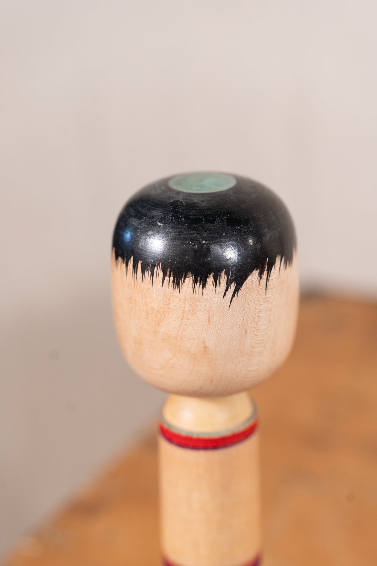 A close-up of a wooden kendo stick with a black lacquered top half, natural wood grain bottom half, and red and black bands near the handle, set against a blurred beige and brown background.