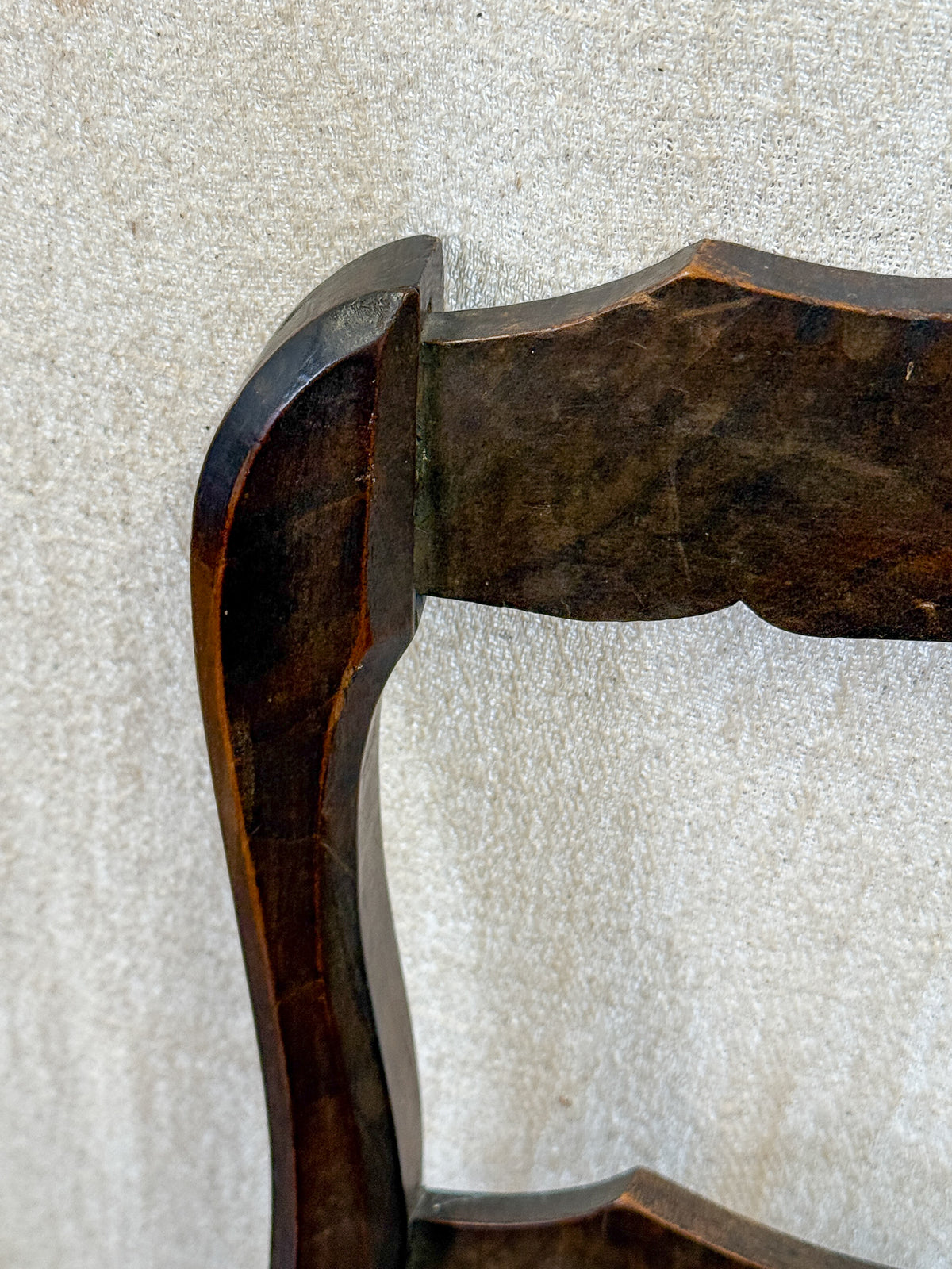 Close-up detail of a dark brown wooden chair backrest corner against a textured light beige fabric background.