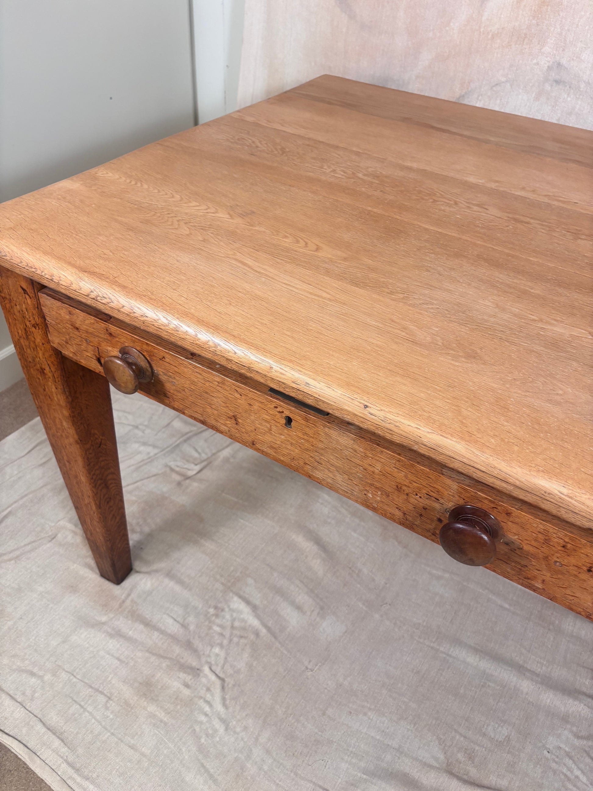 A rustic wooden table with a single drawer, featuring a warm medium-brown finish and round wooden knobs, photographed on a light-colored fabric surface.