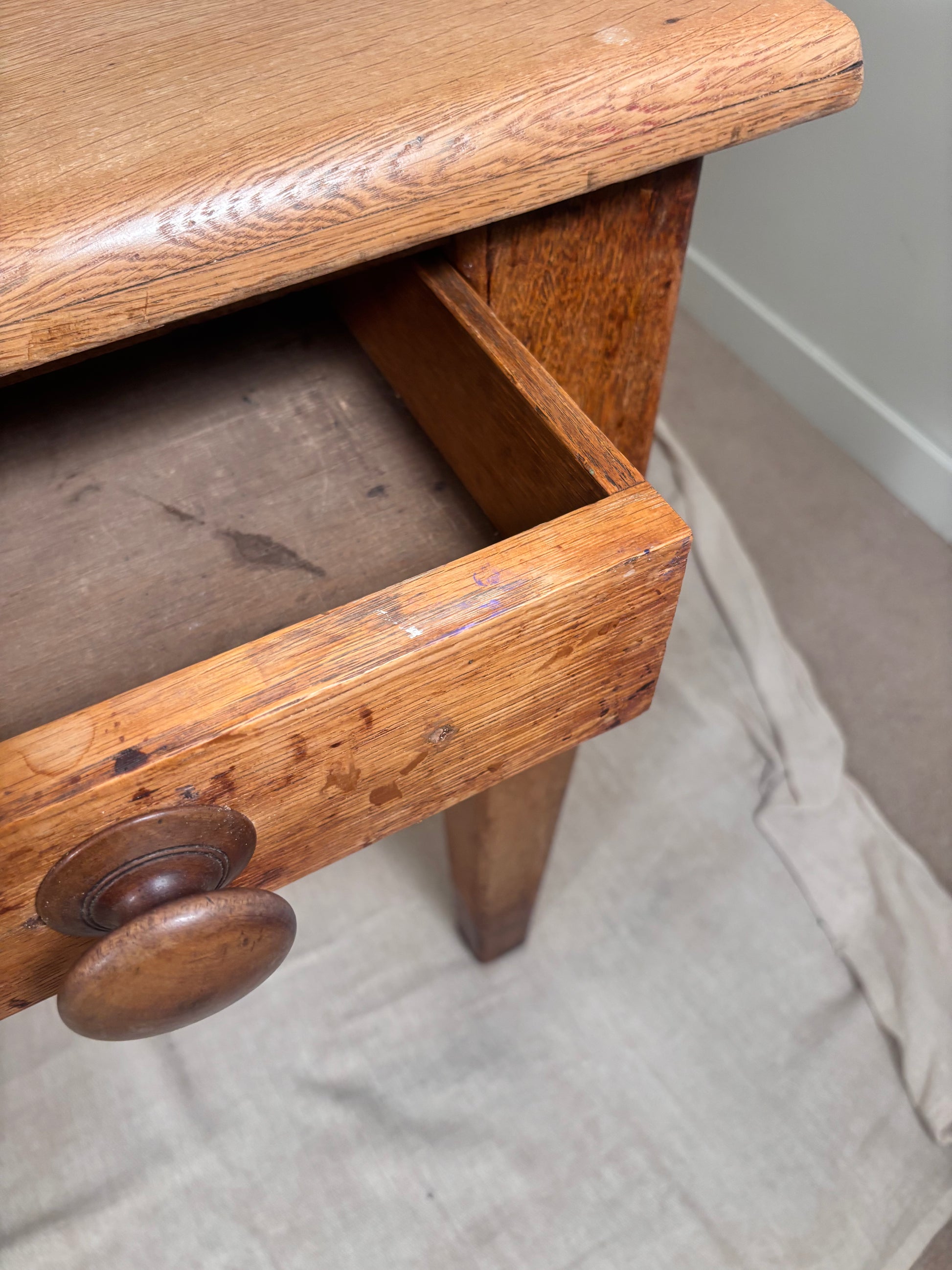Close-up of a rustic wooden side table or nightstand with an open drawer, showing a round wooden knob and the natural wood grain of the oak-like material.