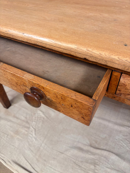 Close-up of a wooden table with a drawer pulled open, showing the wood grain and a round wooden knob, set against a light fabric floor drop.