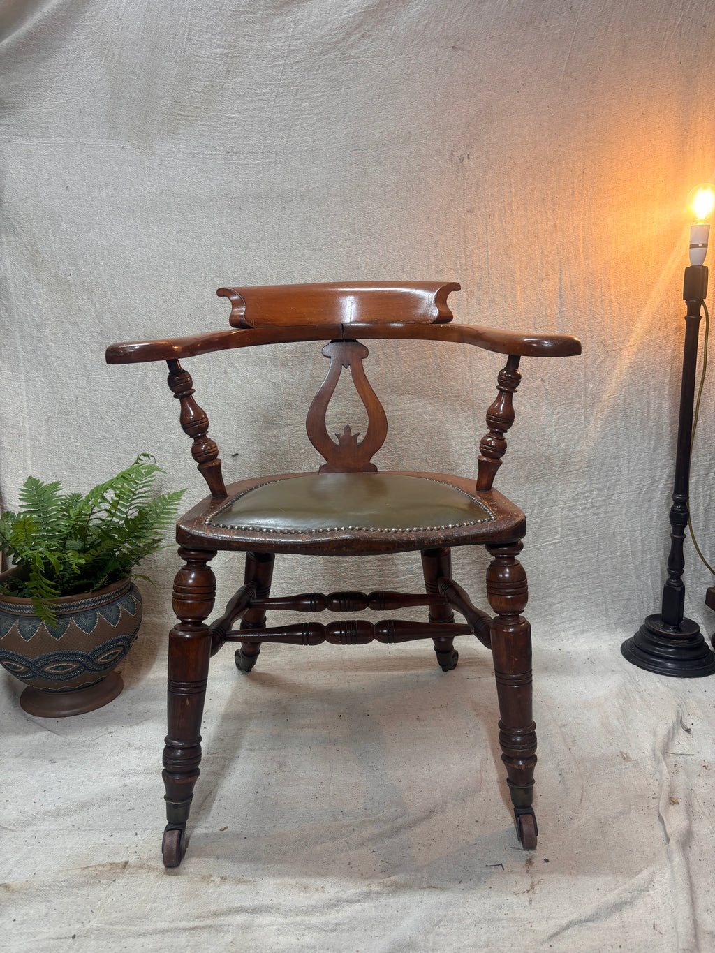 A green leather wooden chair with a lamp and a plant against a plain background