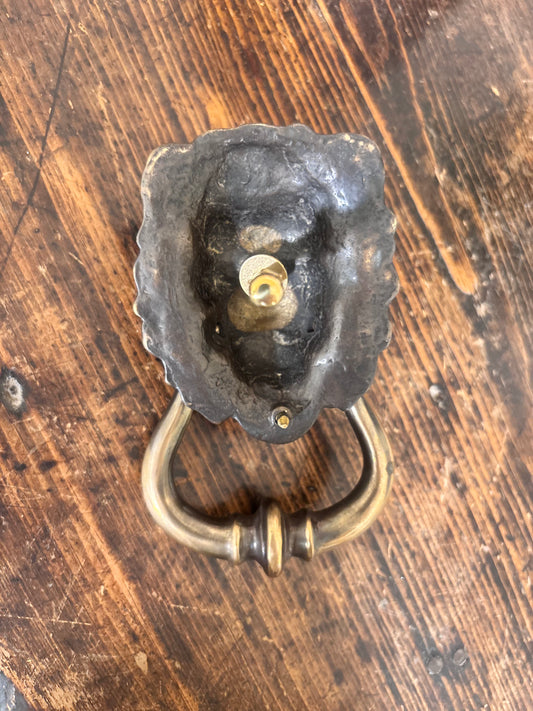 Reverse of a decorative lion head door knocker in an antique brass finish.