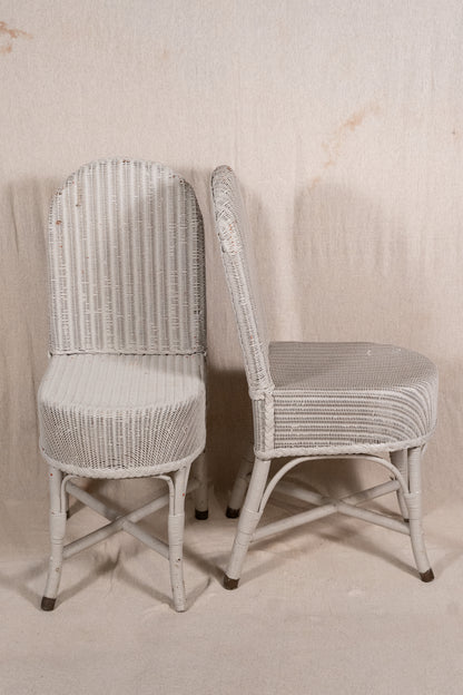 Two white wicker dining chairs with distressed finishes, shown against a neutral beige fabric backdrop.