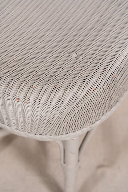 Close-up of a white woven wicker or rattan surface, likely part of a chair or stool, with a matching white frame leg visible below on a light neutral background.