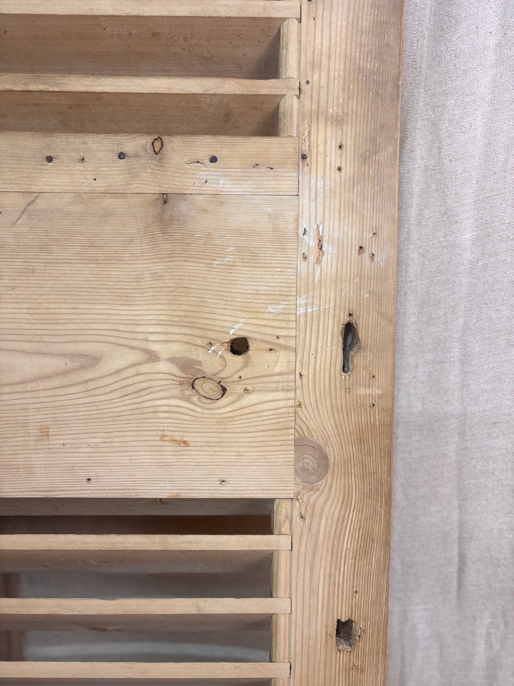 Close-up of a wooden panel with visible grain and texture, next to a gray fabric surface.