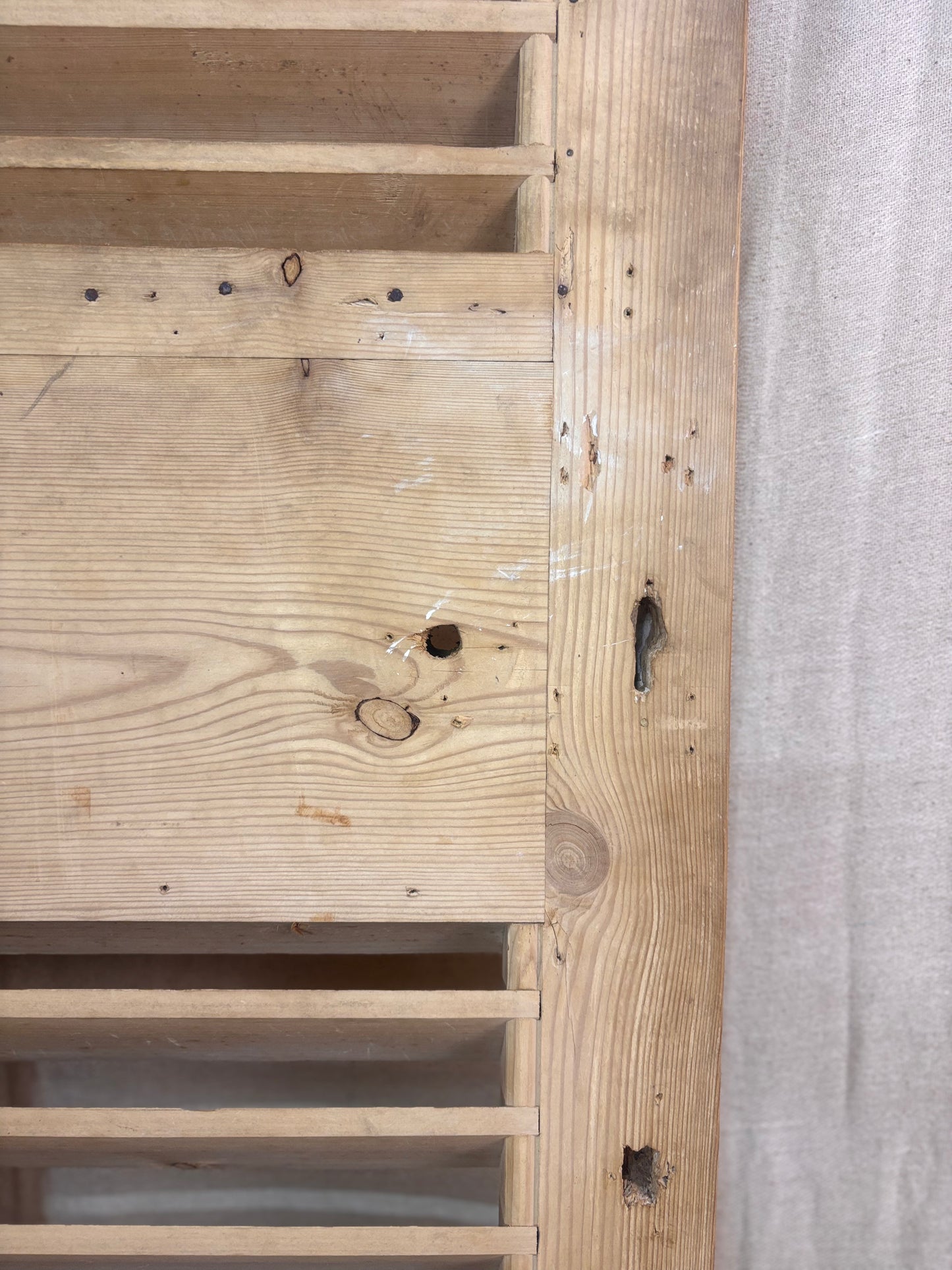 Close-up of a wooden panel with visible grain and texture, next to a gray fabric surface.
