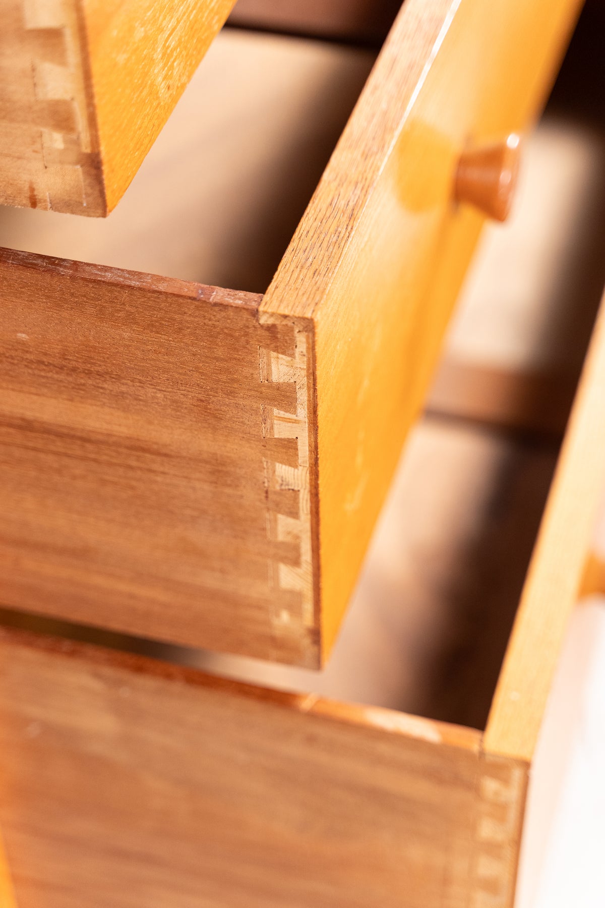 Close-up of a wooden drawer with an open top drawer partially revealing a light-colored interior and a round wooden knob.