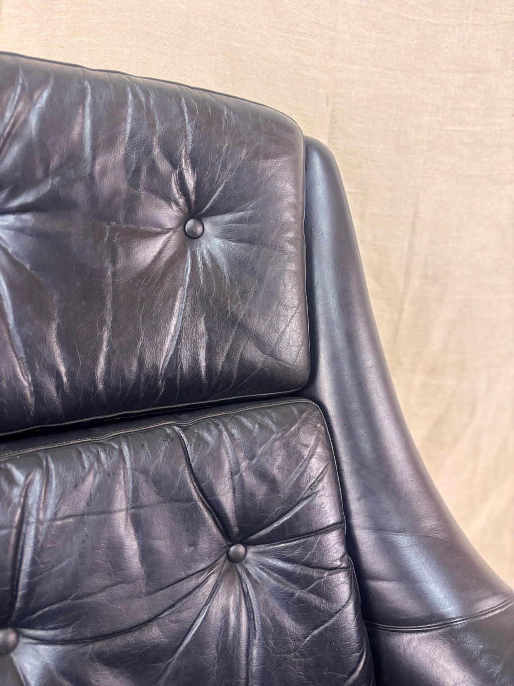 Close-up of a black leather armchair with visible wear on a beige background