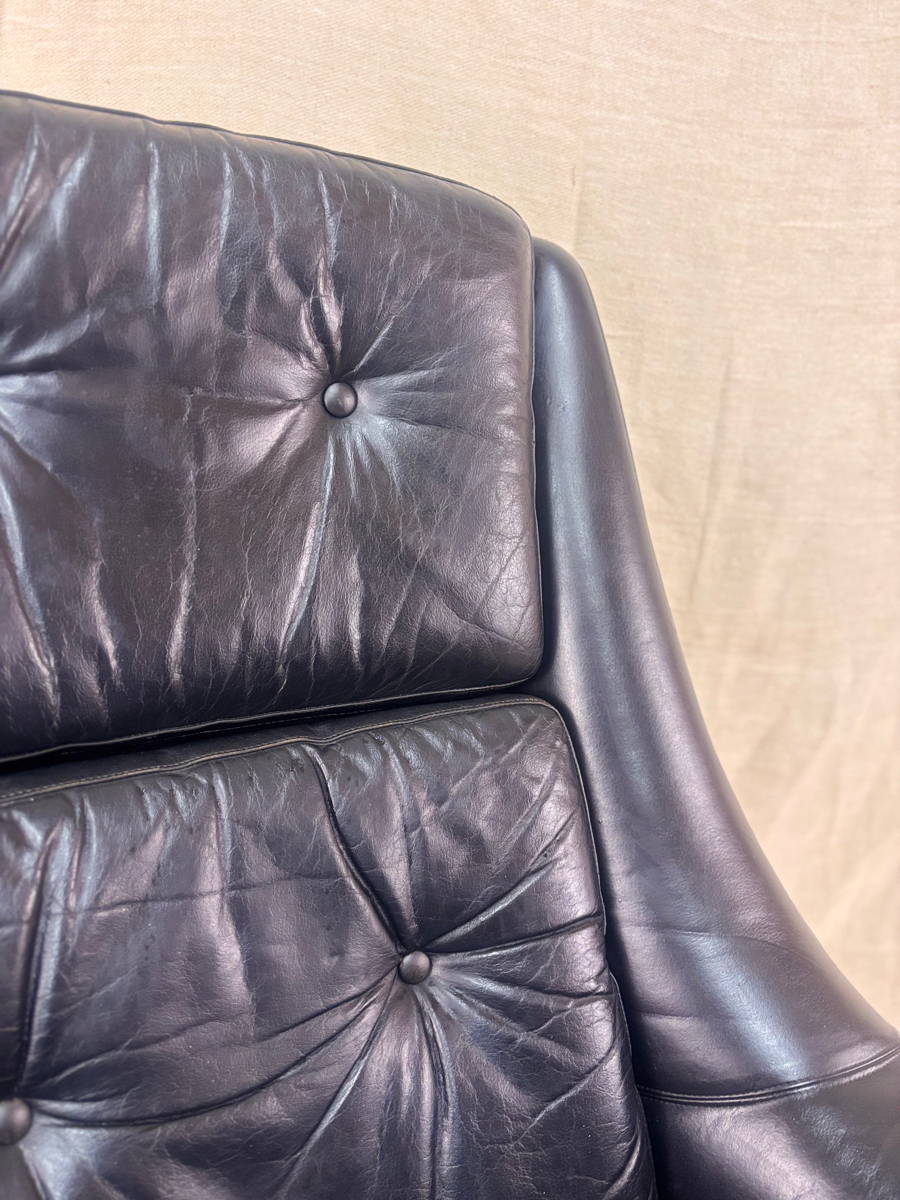 Close-up of a black leather armchair with visible wear on a beige background