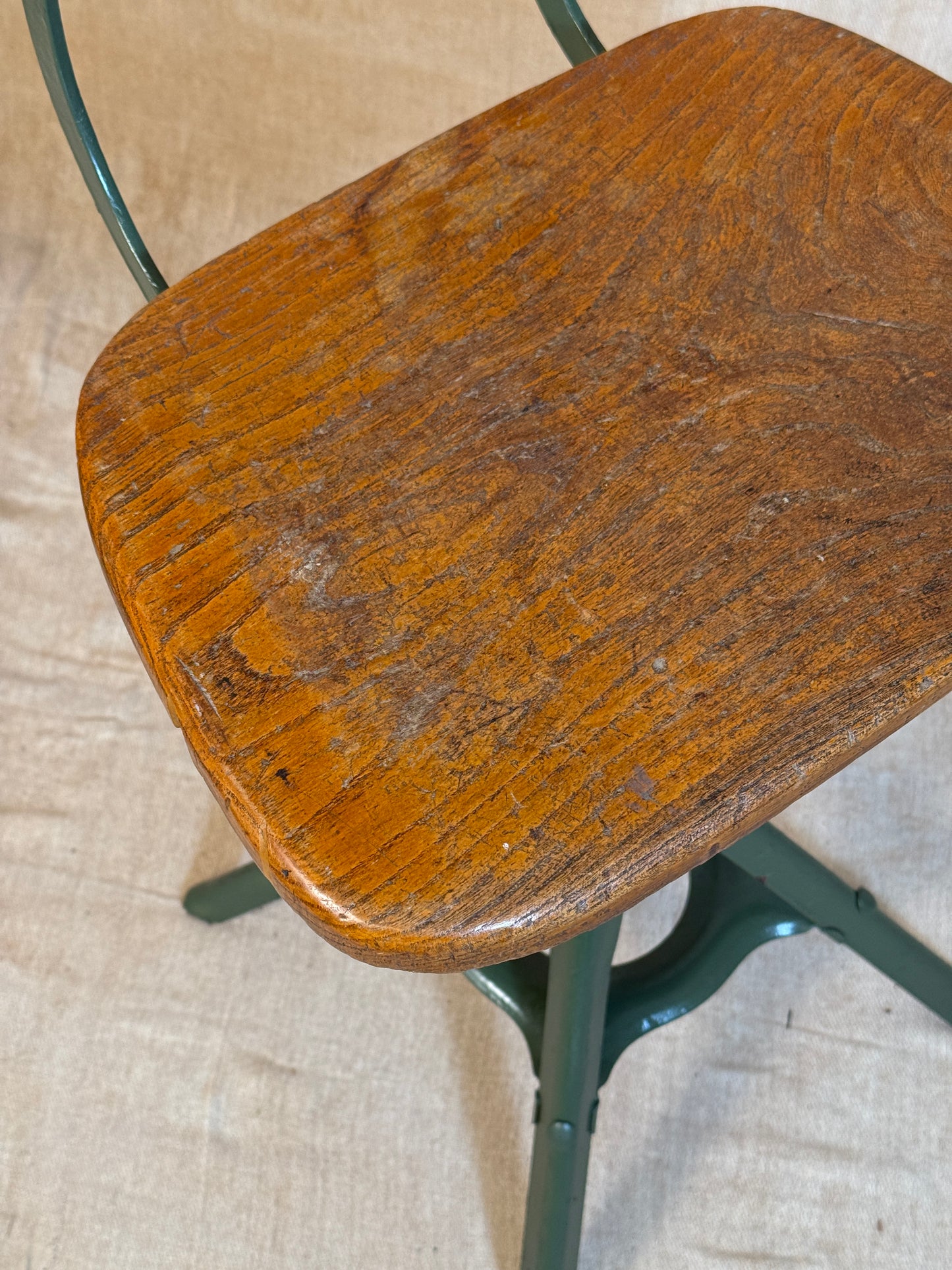 Vintage industrial machinist chair with green steel frame, wooden seat. 