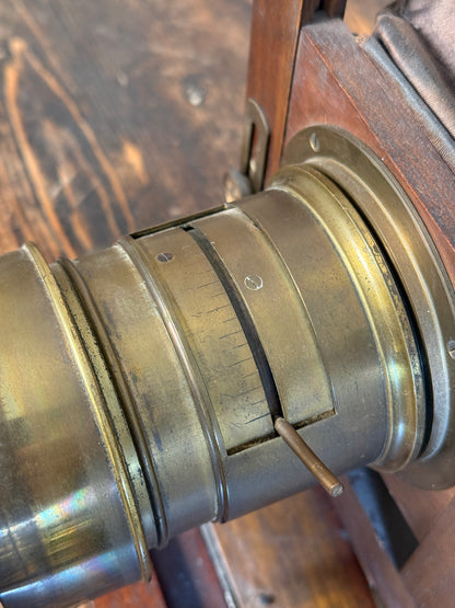 Close-up of a brass camera lens focusing mechanism with a small adjustment screw, set against a dark wooden background.