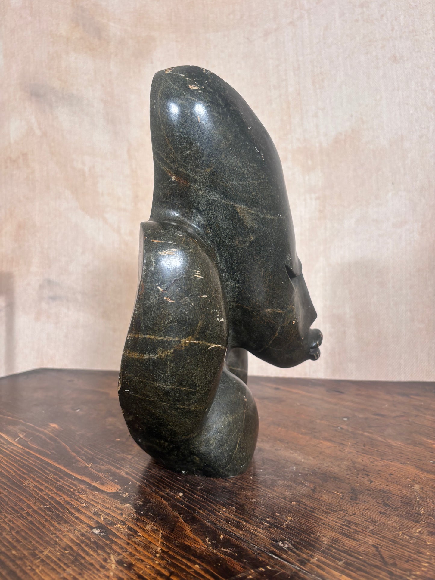 A dark polished stone sculpture of a stylized female head and neck, standing on a wooden surface against a textured beige wall.