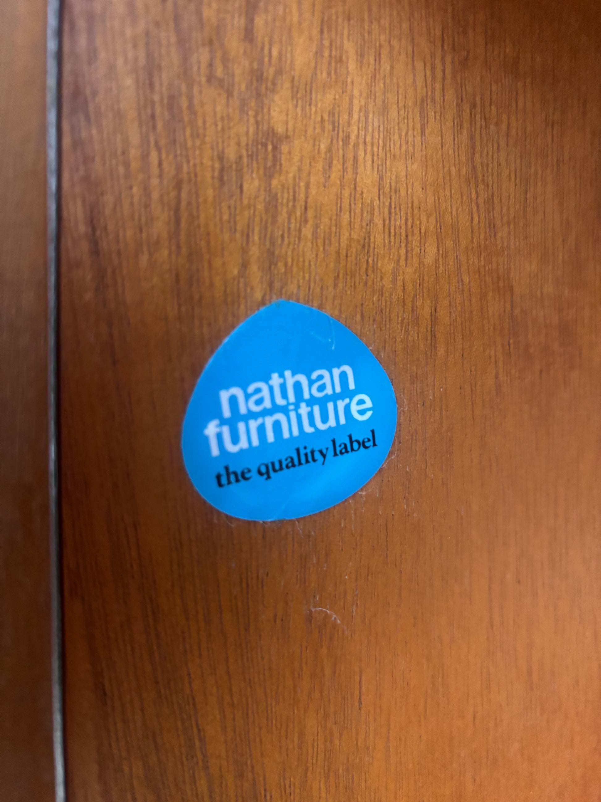 Nathan Furniture Blue sticker on a teak surface with woodgrain