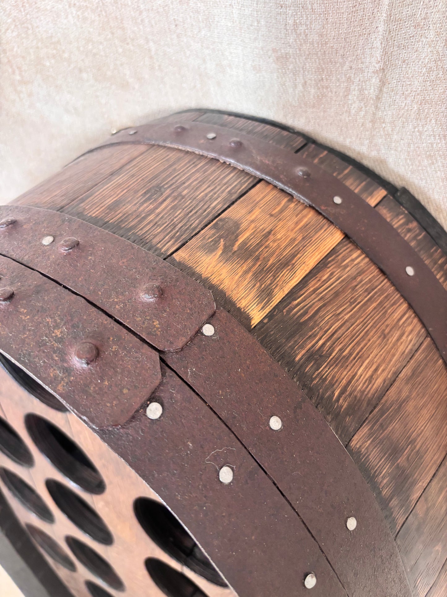Close-up of a decorative barrel-shaped wall piece with dark brown wood panels, weathered metal bands, and rivets against a light beige wall.