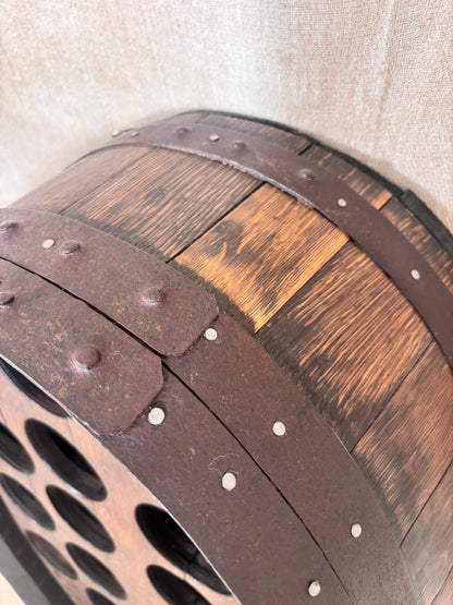 Close-up of a decorative barrel-shaped wall piece with dark brown wood panels, weathered metal bands, and rivets against a light beige wall.