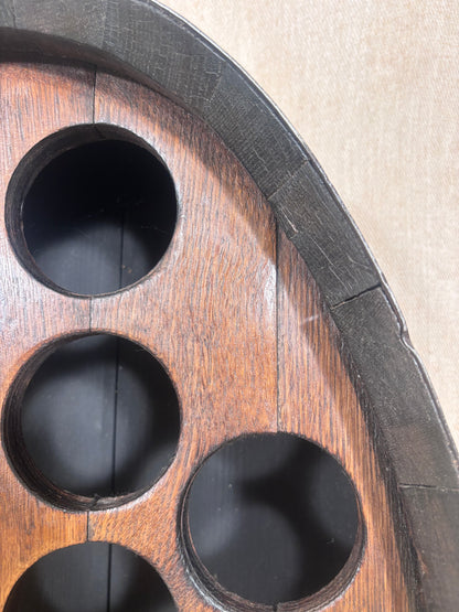 Close-up detail of a wooden circular tray or game board with dark circular cutouts and a dark rim, photographed against a beige background.