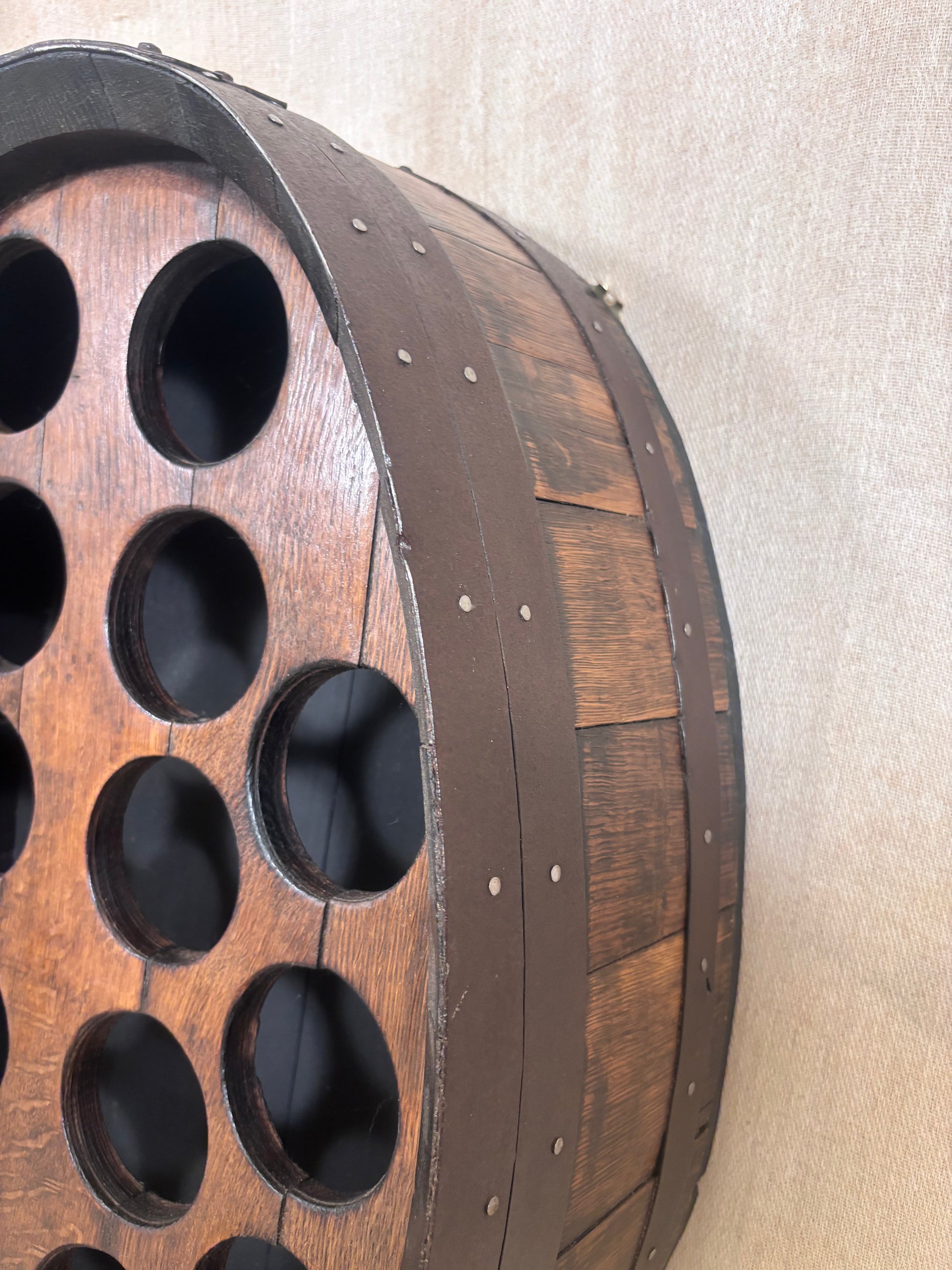A close-up of a rustic wooden barrel-shaped wall decor piece with circular cutouts, mounted against a beige textured wall.