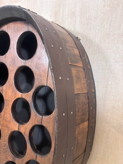 A close-up of a rustic wooden barrel-shaped wall decor piece with circular cutouts, mounted against a beige textured wall.