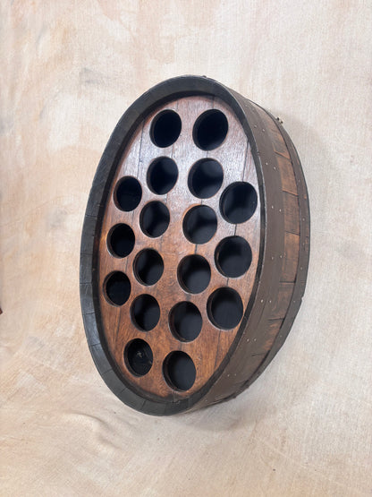 An oval wooden wall-mounted wine bottle rack made from a repurposed barrel, featuring a dark brown stained wood body, dark metal bands, and multiple circular cutouts for bottles.