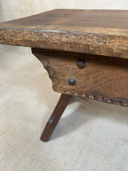 Close-up of an antique wooden table showing the corner joint, carved apron, two dark metal drawer knobs, and a turned leg on a beige fabric background.