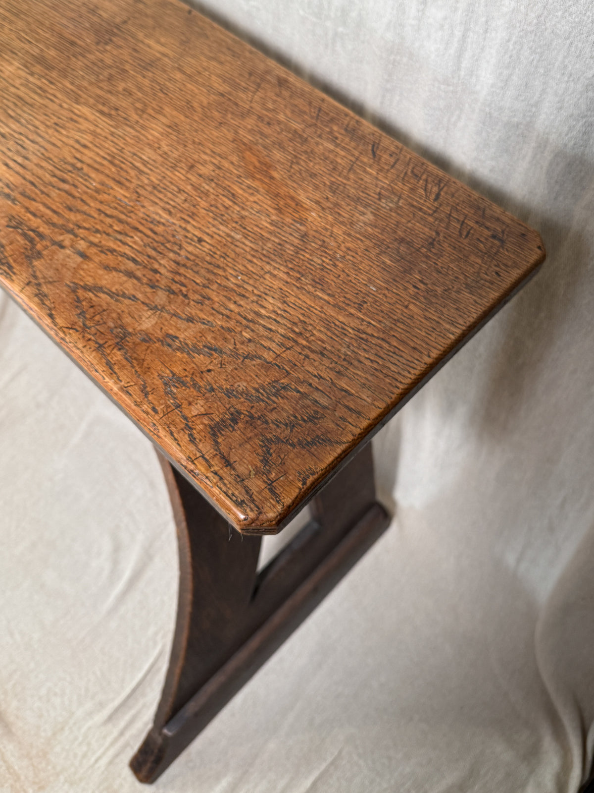 Traditional oak organ bench in the Gothic style, with a wide wooden seat and angled side frames. 
