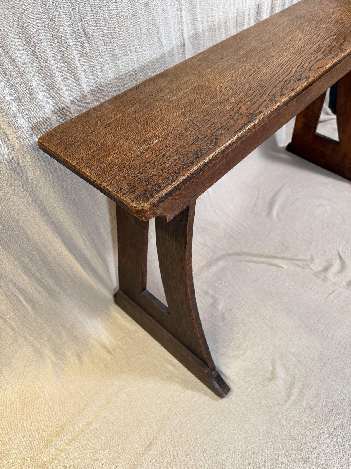 Traditional oak organ bench in the Gothic style, with a wide wooden seat and angled side frames. 
