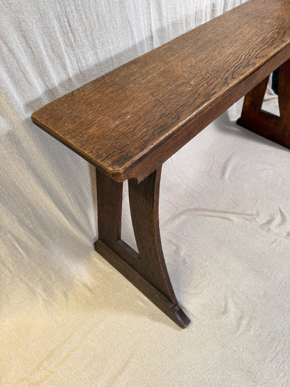Traditional oak organ bench in the Gothic style, with a wide wooden seat and angled side frames. 
