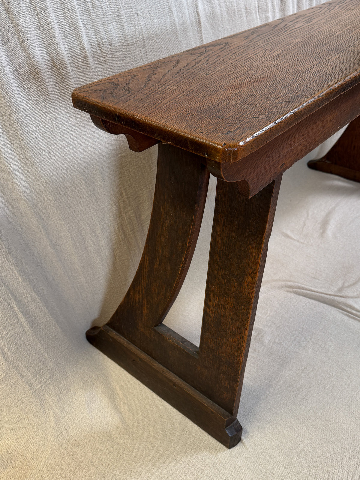 Traditional oak organ bench in the Gothic style, with a wide wooden seat and angled side frames. 