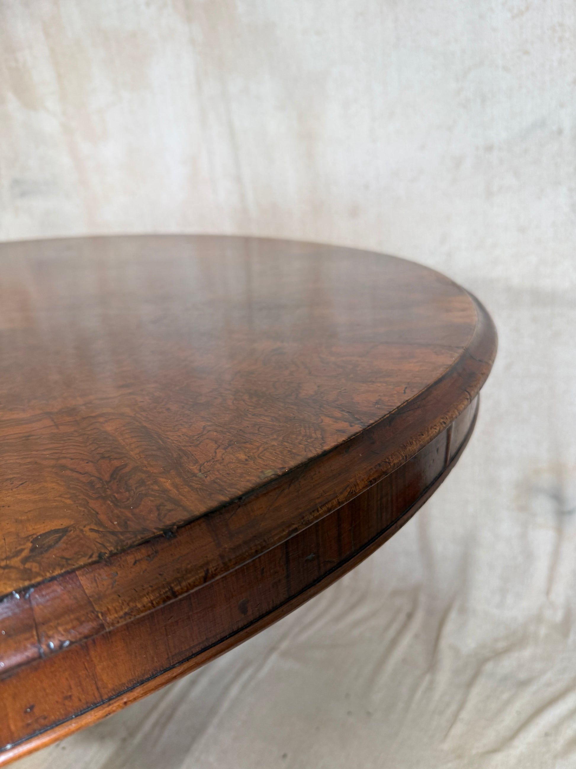 Close-up of a round wooden table top with a rich brown grain and a raised rim, photographed against a light fabric backdrop.