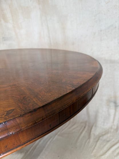 Close-up of a round wooden table top with a rich brown grain and a raised rim, photographed against a light fabric backdrop.