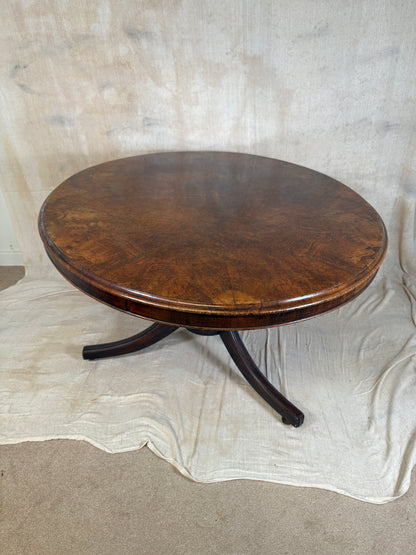 A round wooden table top with a dark brown polished finish and three curved legs, photographed on a draped off-white cloth over a concrete floor.
