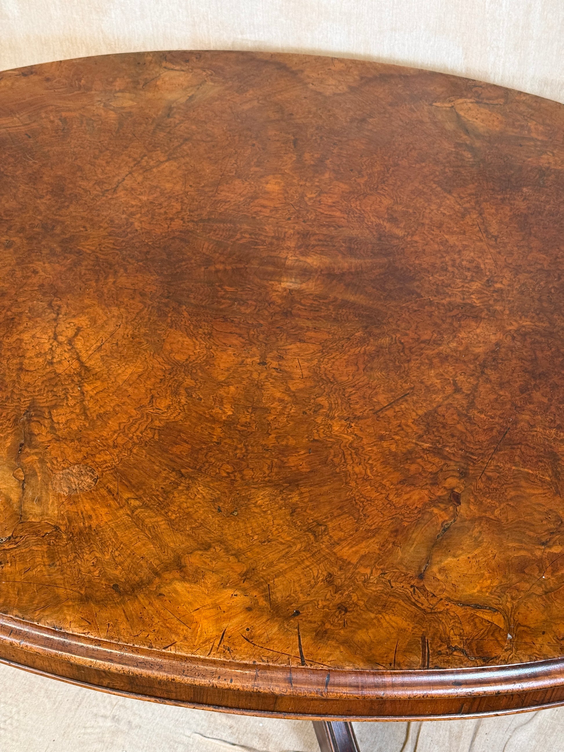 Close-up of an oval wooden tabletop with a rich warm brown finish and visible wood grain, showing part of the curved rim and a light neutral surface around it.