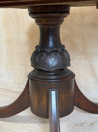 Close-up of a dark brown carved wooden table pedestal base with a metal bar extending from the side, set against a light beige tiled background.